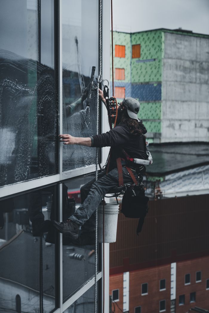 Un homme, harnaché, nettoie avec précision les vitres d’un gratte-ciel.